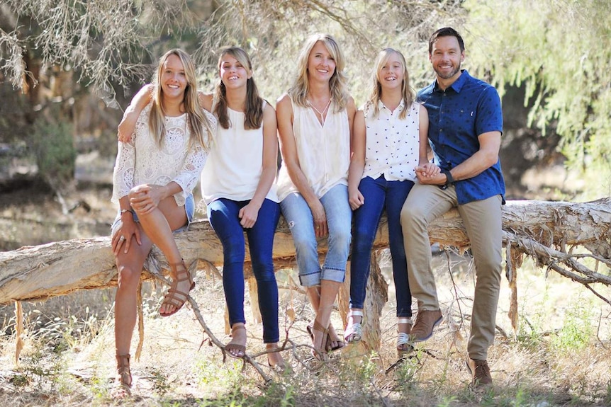 A family including three girls poses for a photo sitting on a tree log.