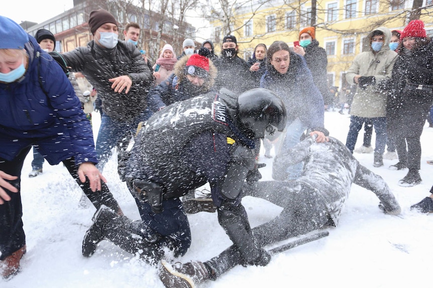 A policeman detains a protesters who is on the ground in the snow, while protesters try to help him.
