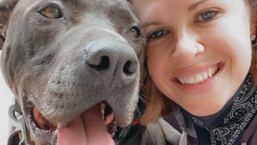 A young woman smiles as she poses for a selfie with a large grey dog with it's tongue hanging out.