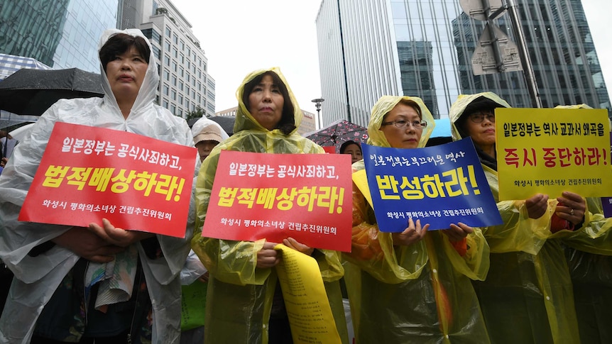 Women in raincoats hold signs