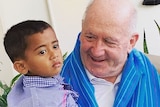 Sir Peter Cosgrove smiles at a young boy he is holding. The boy is looking off into the distance.