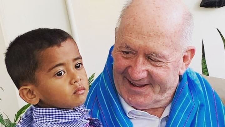 Sir Peter Cosgrove smiles at a young boy he is holding. The boy is looking off into the distance.