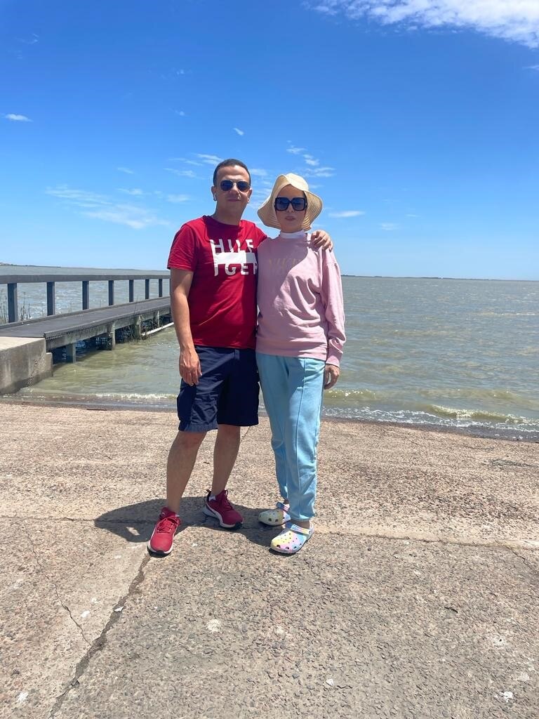 Two people standing near a jetty along a beach.