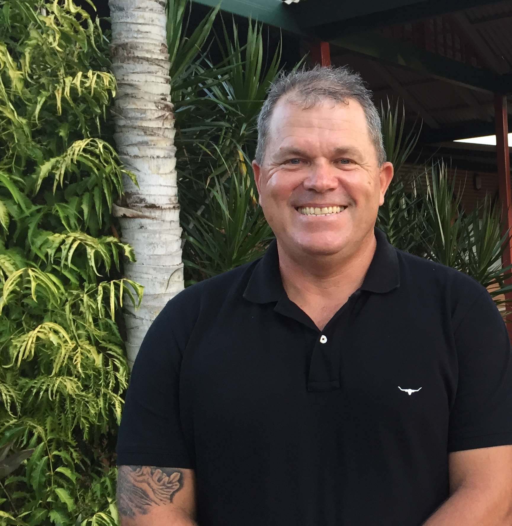 A smiling man with short gray hair, wearing a dark shirt.