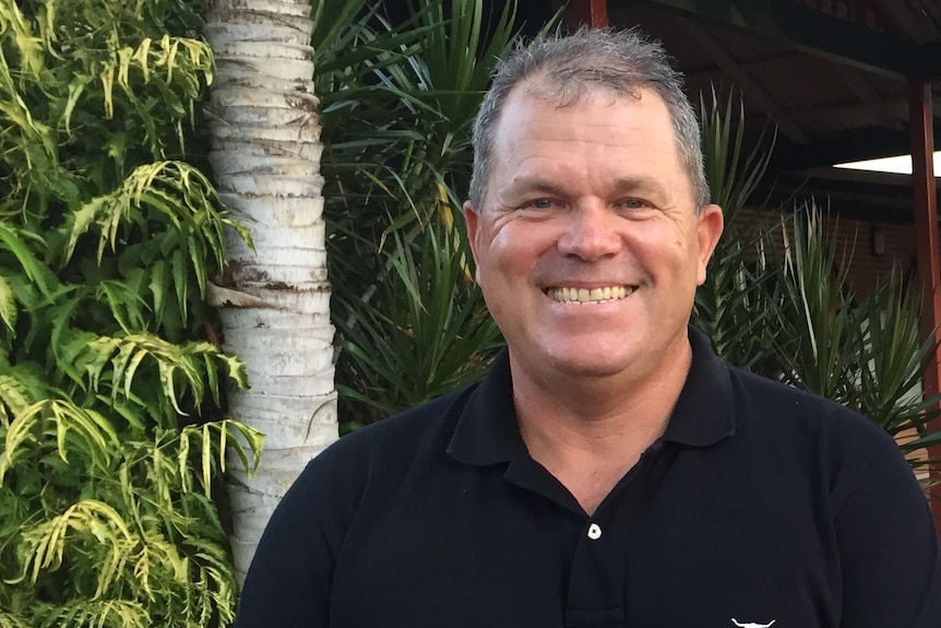 Man with short grey hair and black shire smiling at the camera.