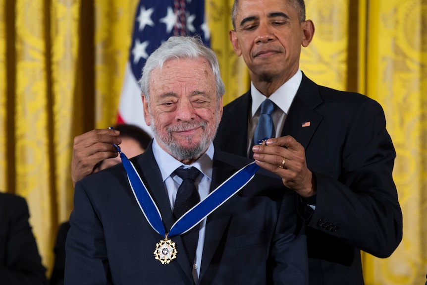 Barack Obama stands behind Stephen Sondheim and holds a medal to him