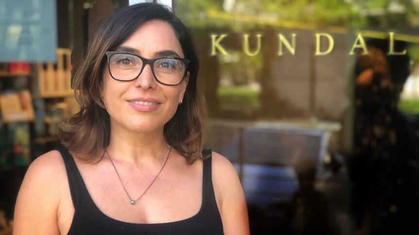 Susie Dimov stands in front of a window outside her salon with the word "Kundalini" in gold print