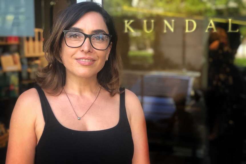 Susie Dimov stands in front of a window outside her salon with the word "Kundalini" in gold print