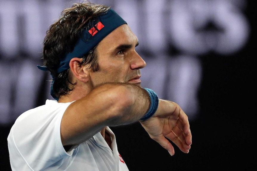 Roger Federer wipes his chin as he waits to play against Taylor Fritz at the Australian Open.