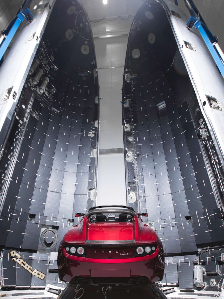 A red convertible sports car sits on a conical base inside an opened cylinder.