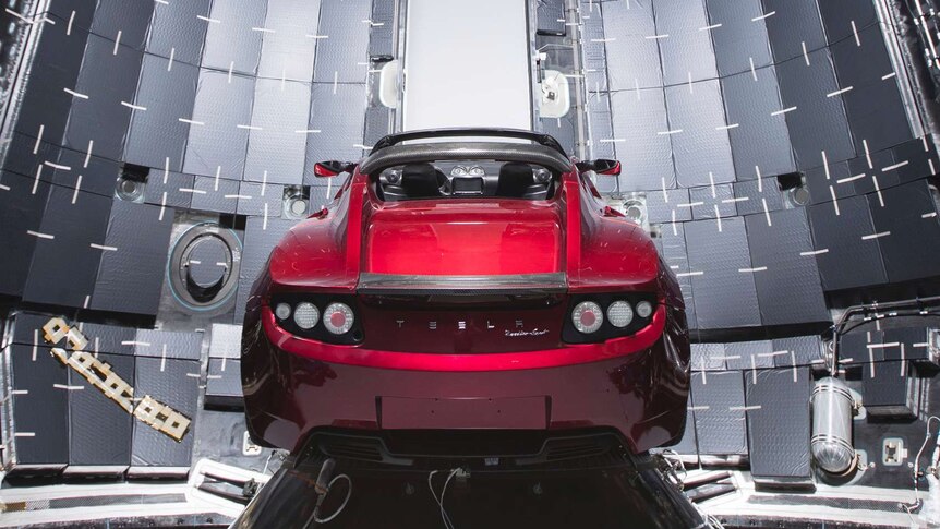 A red convertible sports car sits on a conical base inside an opened cylinder.
