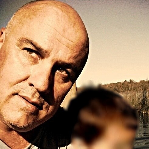 A man looks out to the side of the camera, a child in his lap has been blurred out