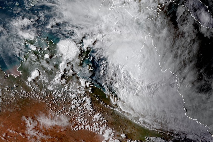 Cyclone Trevor is seen from a birds' eye view as white cloud off the coast of NT. The land next to it is green and orange desert