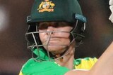 Steve Smith holds his bat above his head and looks behind him wearing yellow cricket kit