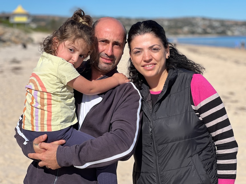 A man and a woman holding a child in front of a beach