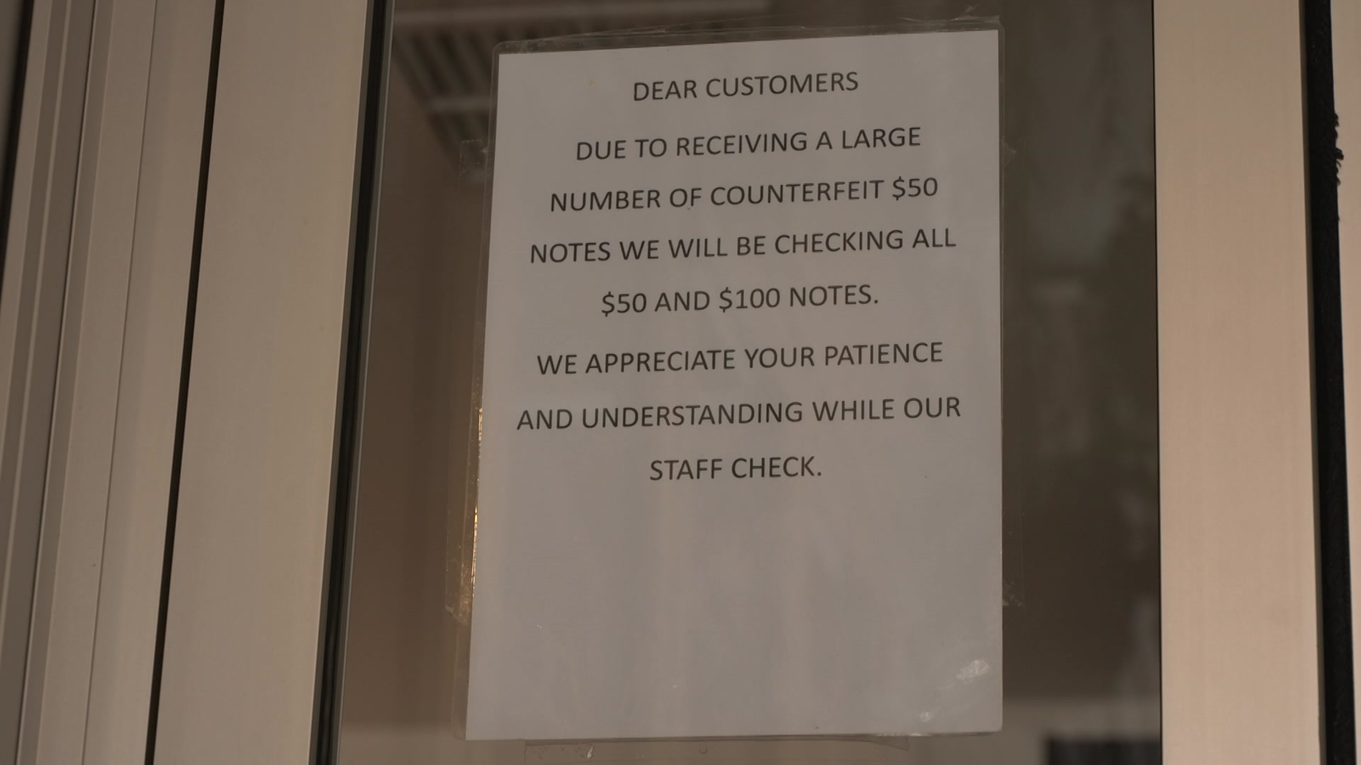 A white sign on a glass shop door which tells visitors about the increasing use of counterfeit money
