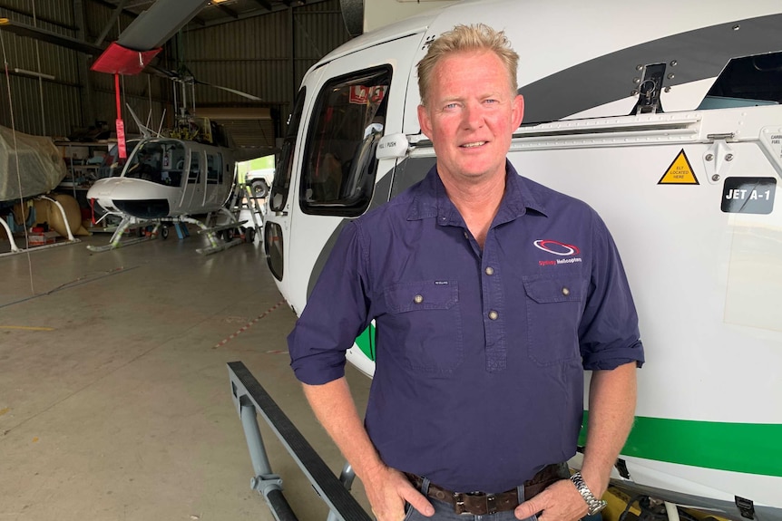 Caucasian man stands in front of a helicopter.