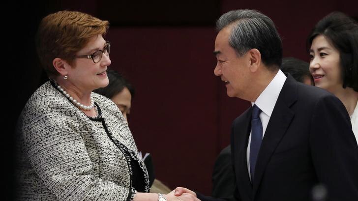 Marise Payne, left, wears a black and white jacket with pearls at her neck as she shakes the hand of Wang Yi, in a suit.