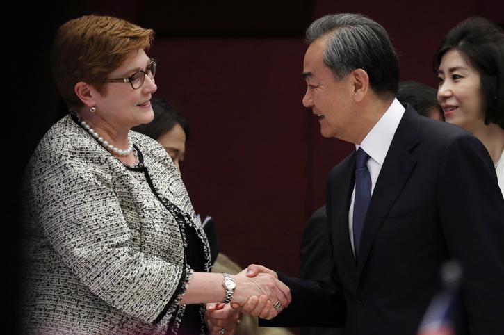 Marise Payne, left, wears a black and white jacket with pearls at her neck as she shakes the hand of Wang Yi, in a suit.