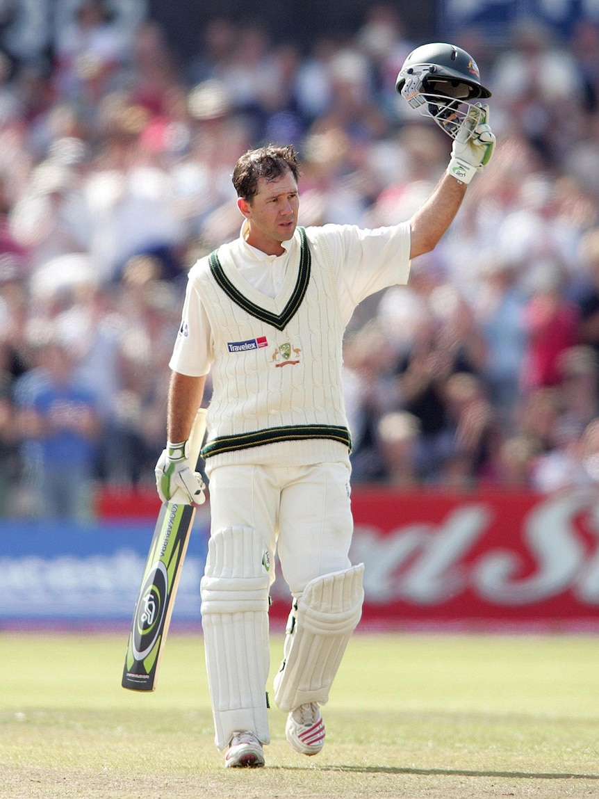 A man in cricket whites raises his helmet in the air.