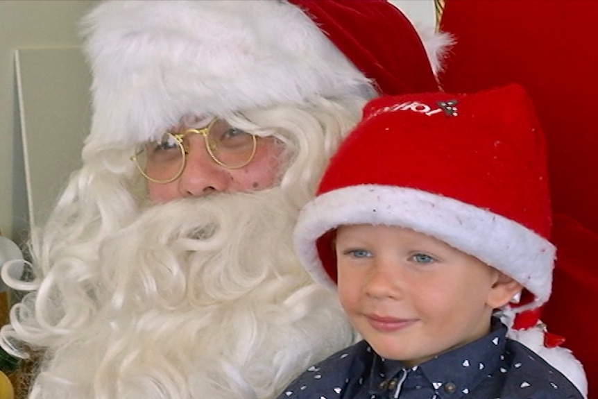 A young boy sits on signing Santa's knee