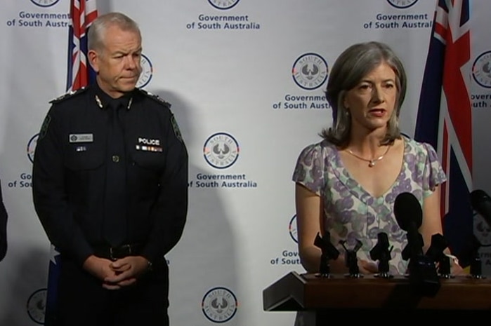 A man in a police uniform, a woman at a dais with microphones and an Auslan interpreter