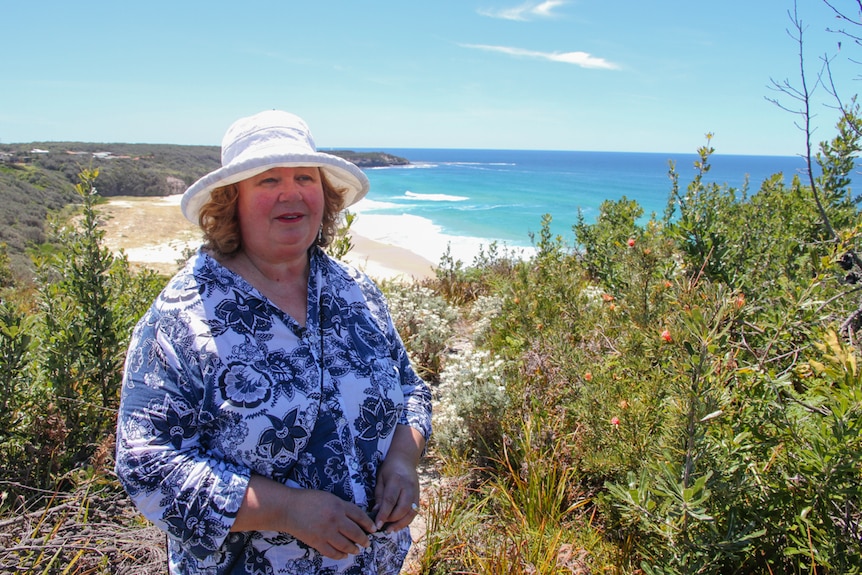 A woman stands on a heath headland with her back to the beach