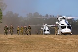 A group of army personnel walk away from two white army helicopters in the middle of a field