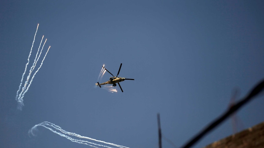 An Iraqi Army helicopter launches decoy flares in the sky above buildings
