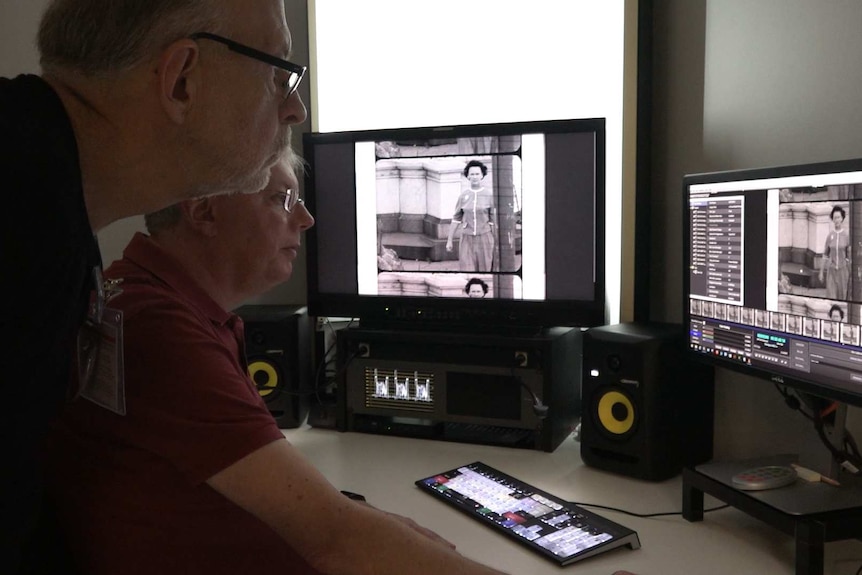 A man leans over a computer monitor showing black-and-white footage of a woman in the street.