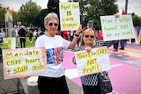 two ladies hold up signs highlighting the attention aged care needs