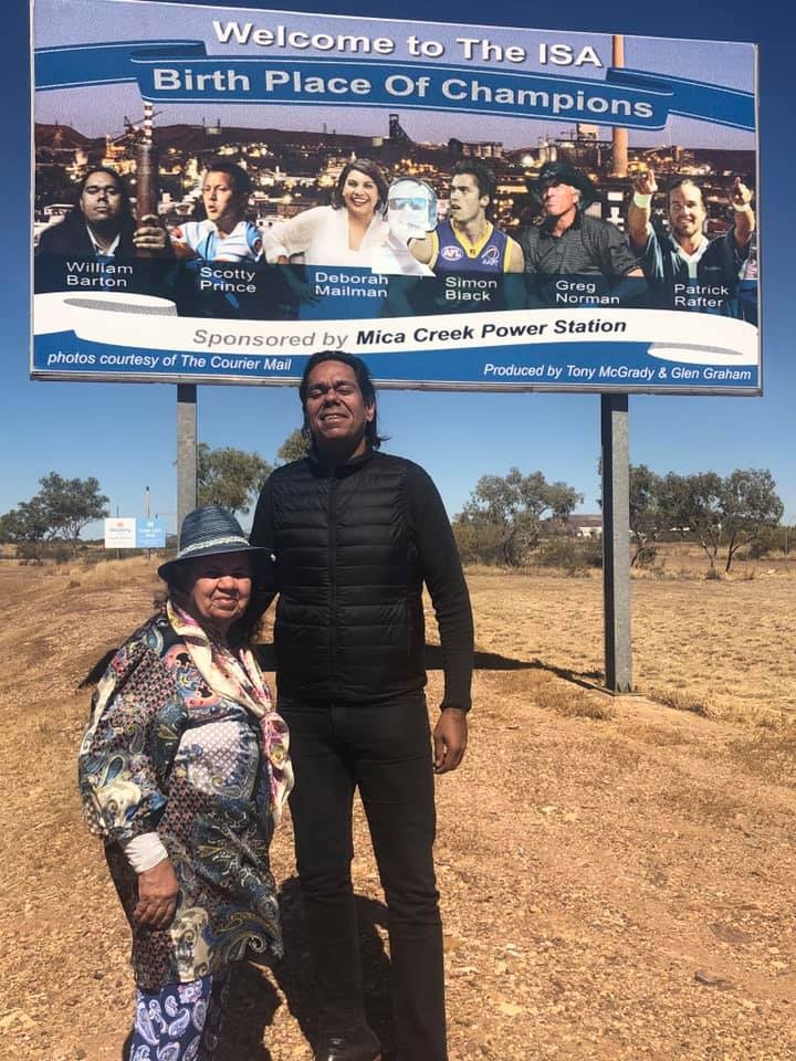 A woman and a much taller man stand in front of a sign reading Welcome to Mt Isa