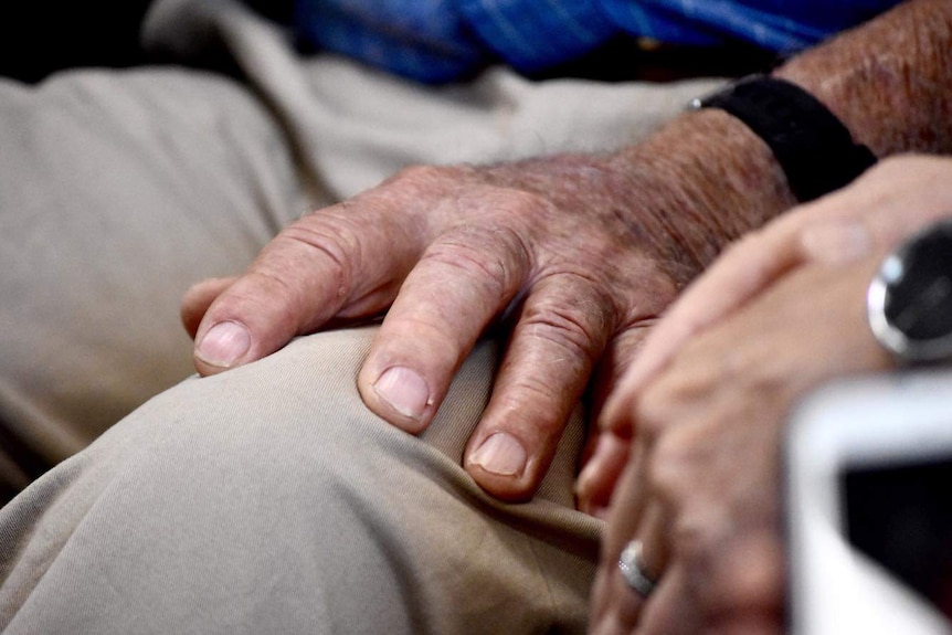 Close up of an elderly man's hand resting on his knee.