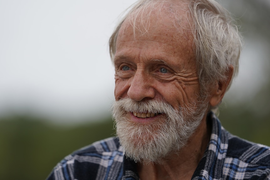 Headshot of a 77-year-old man with grey hair and beard, smiling