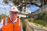 Man wearing a hard hat and high-vis vest standing in front of a building.