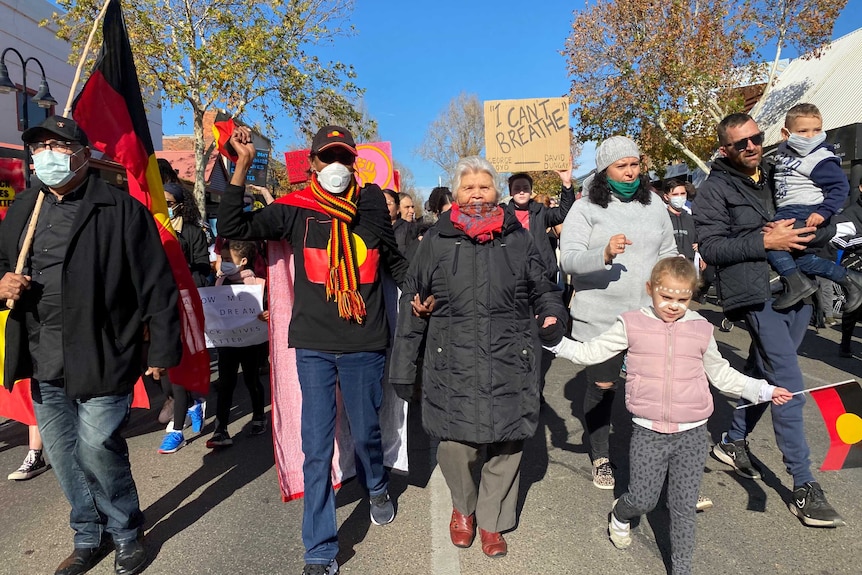 Protesters walk down a road as they hold Aboriginal flags.