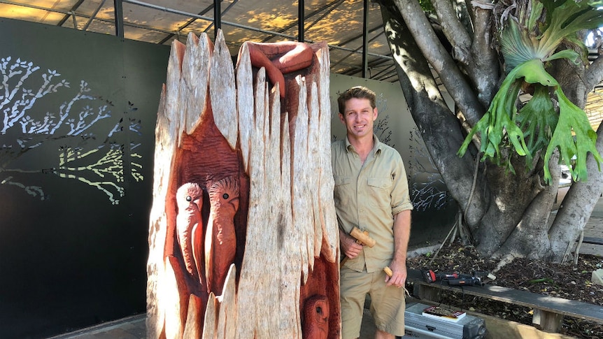 A man stands next to a carved log