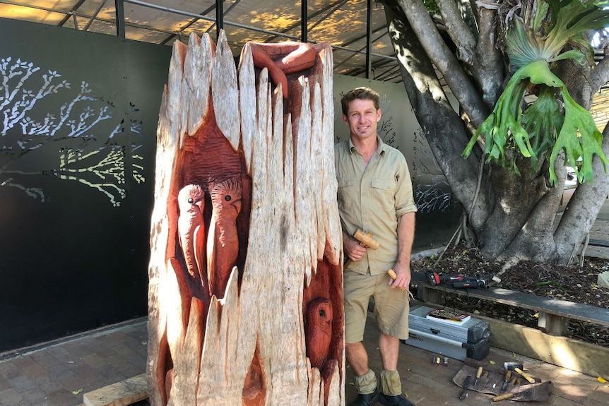 A man stands next to a carved log