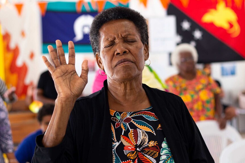 A woman with her eyes closed and hand raised in church.