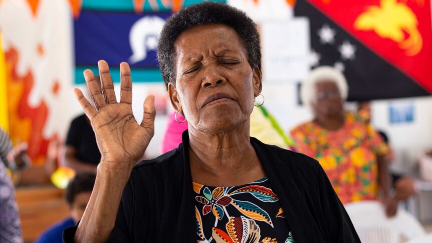 A woman with her eyes closed and hand raised in church.