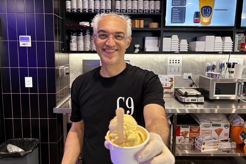 A man, wearing a black T-shirt, holds out a cup of yellow ice cream