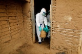 A healthcare worker in a hazmat suit removes items from a woman's house.