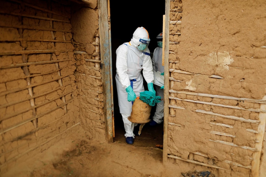 A healthcare worker in a hazmat suit removes items from a woman's house.