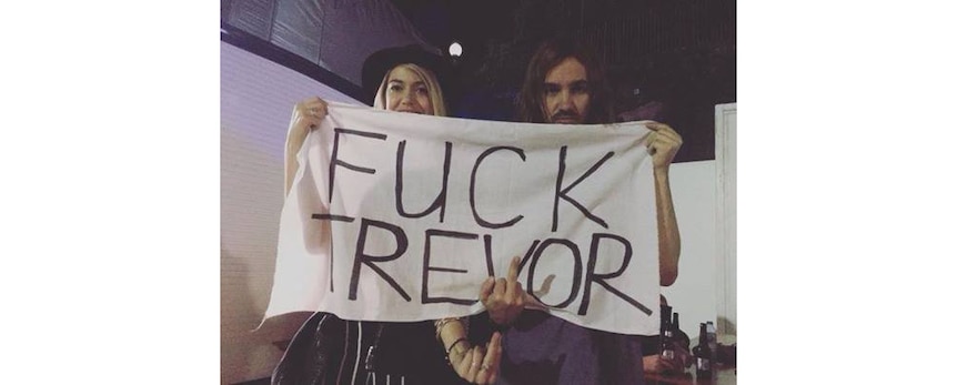 Tame Impala's Kevin Parker and his partner Sophie holding up a banner that reads 'Fuck Trevor'