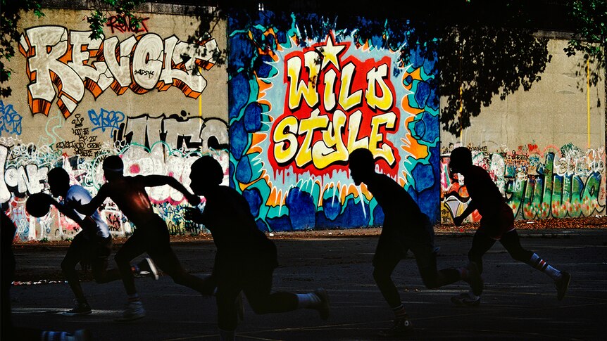 Silhouette of five running basketballers on concrete court in front of brightly styled graffitied wall.