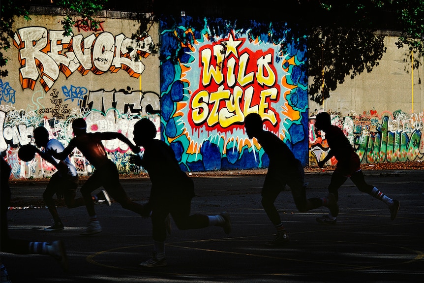 Silhouette of five running basketballers on concrete court in front of brightly styled graffitied wall.