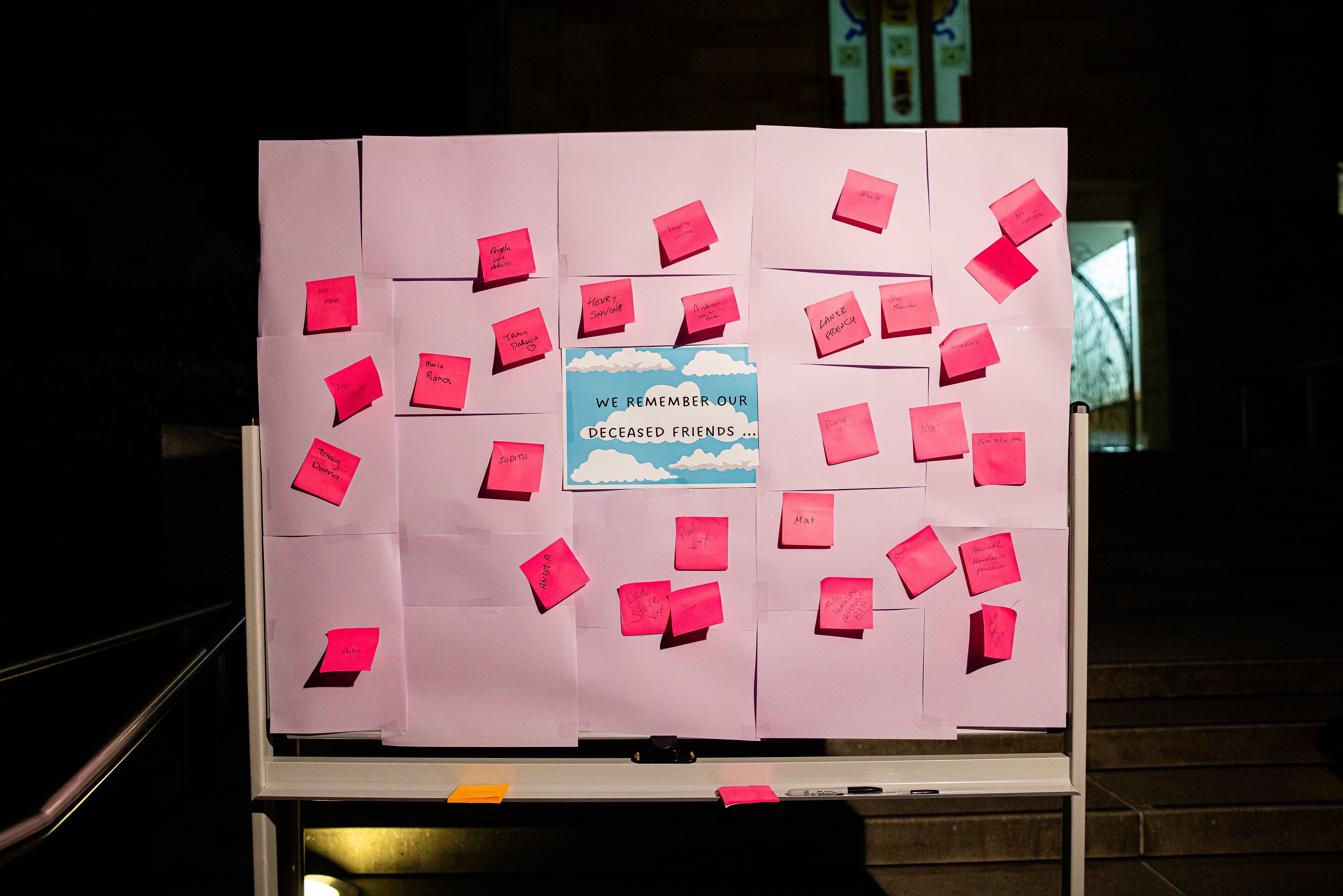 Purple%20board%20with%20pink%20sticky%20notes%20with%20names%20written%20on%20them.%20Sign%20says%20We%20remember%20our%20deceased%20friends