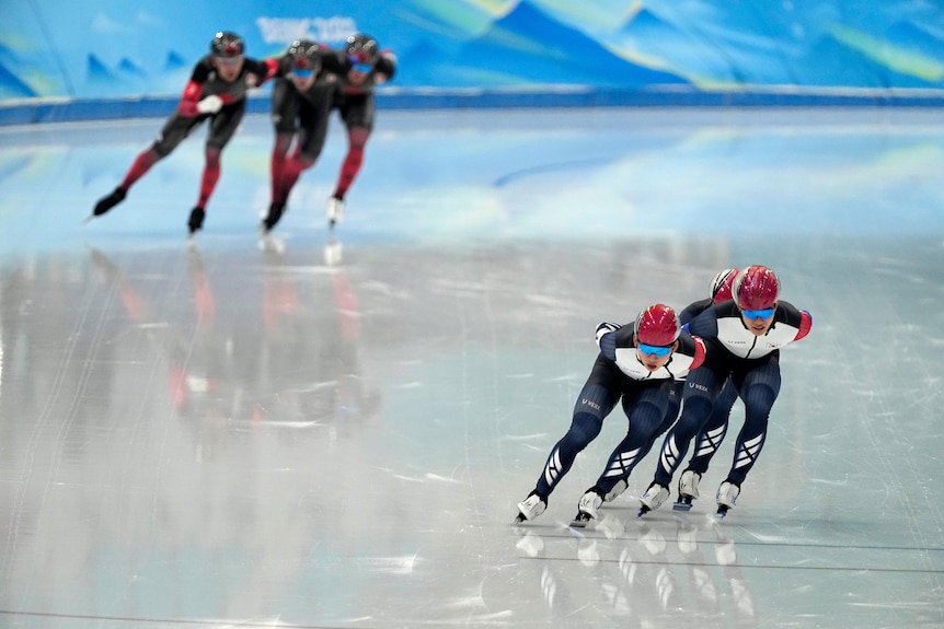 South Koreas speed skaters in the foreground skate away from Canadians, blurry in the background.