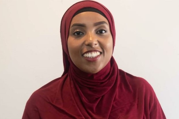 Amina Liban smiles wearing a red hijab and mustard floral dress.