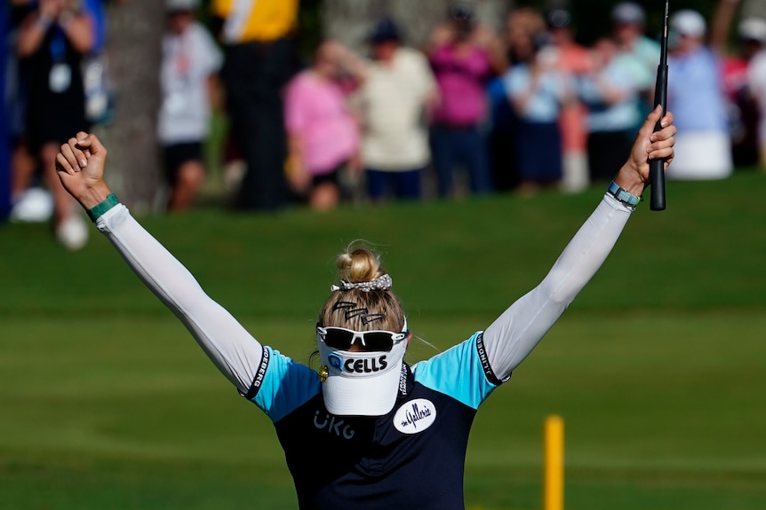Nelly Korda lowers her head and holds her arms in the air